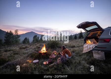 Donna che viaggia in auto e ha un picnic in montagna Foto Stock