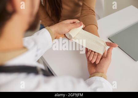 Infermiera presso l'ufficio medico che fornisce il pronto soccorso applicando un bendaggio sul polso del paziente Foto Stock