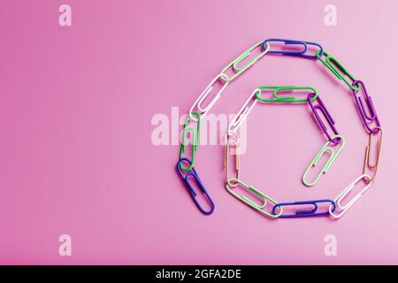 Una catena di graffette in carta multicolore su sfondo rosa. Concetto di comunicazione e cooperazione commerciale Foto Stock