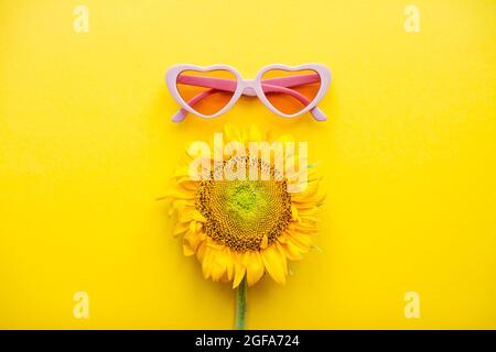 Disposizione di occhiali da sole rosa a forma di cuori e girasoli su uno sfondo giallo brillante Foto Stock