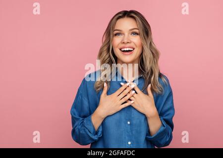 Grata felice femmina felice con bocca aperta che tiene le mani al petto sensazione di gratitudine e toccato Foto Stock