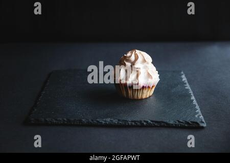 Muffin al ribes decorato con crema alla vaniglia su sfondo nero. Appetitoso muffin freschi alla vaniglia su tavola scura Foto Stock