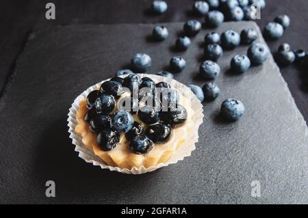 Crostata con mirtilli è su uno sfondo nero di pietra naturale. Ancora vita con dolci dolci con frutti di bosco su sfondo scuro Foto Stock