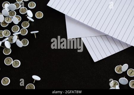 Materiale per ufficio come alcuni fogli di carta e altri articoli di cancelleria bianca su un tavolo di legno nero Foto Stock