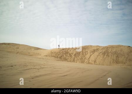 Lone figura (uomo) in piedi sulla cima di grandi dune di sabbia durante il giorno d'inverno Foto Stock