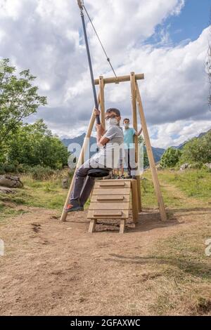 i bambini che indossano le maschere giocano su una zip line in un parco giochi nel campo estivo, verticale Foto Stock