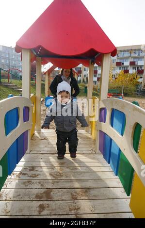 POZNAN, POLONIA - 01 novembre 2015: Un adorabile ragazzino che cammina su un ponte di legno con la sua mummia in un parco giochi a Poznan, Polonia Foto Stock