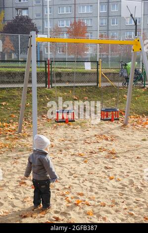 POZNAN, POLONIA - Nov 01, 2015: Un piccolo bambino carino in piedi da un altalena ambientato in un parco giochi a Poznan, Polonia Foto Stock