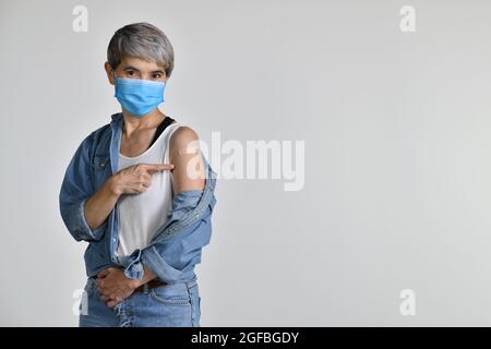 Donna asiatica di mezza età vaccinata puntando il dito sul cerotto adesivo sul braccio dopo iniezione antivirale di coronavirus isolato su whit Foto Stock