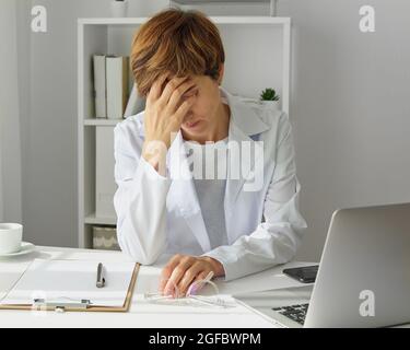 Operatore sanitario femminile che ha mal di testa. Medico stanco e stressato. Lati negativi del lavoro duro Foto Stock