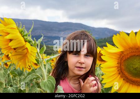 ragazza giovane e sorridente tra girasoli in un paesaggio montano. Foto Stock