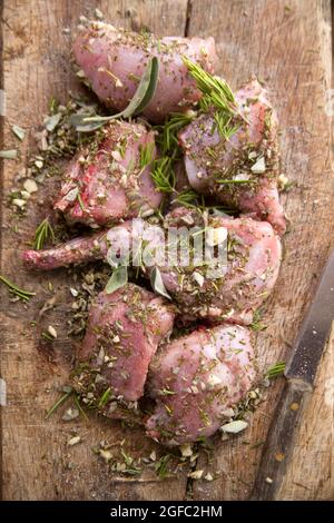 Preparazione con erbe aromatiche mediterranee tritate di porzioni di coniglio crudo Foto Stock