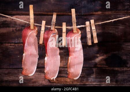 Presentazione di fette di pancetta appese ad un filo con pinzette Foto Stock
