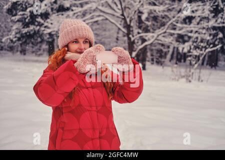 Una donna felice tiene un telefono cellulare nelle sue mani, un parco invernale con alberi nella neve Foto Stock