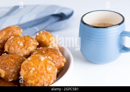 le chouquettes francesi puffs con perle di zucchero sul piatto con la tazza blu di caffè. Pasticceria Choux panetterie francesi classiche. Foto Stock