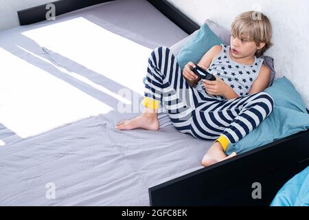 Ragazzo che tiene il controller di gioco joystick nelle mani, giocando a videogame a casa. Foto Stock