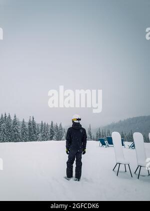 Vista posteriore di uno sciatore in cima ad una montagna che guarda all'orizzonte la foresta di abeti ricoperta di neve. Giornata invernale nevosa presso la stazione sciistica di Bukovel, Ucraina Foto Stock