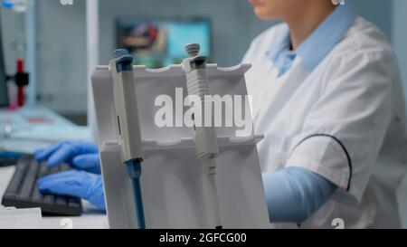 Primo piano di biochimici che utilizzano micropipette in laboratorio per analisi scientifiche nell'industria sanitaria. Medico professionista in camice da laboratorio con contagocce per liquidi su scrivania utilizzato per lo sviluppo Foto Stock