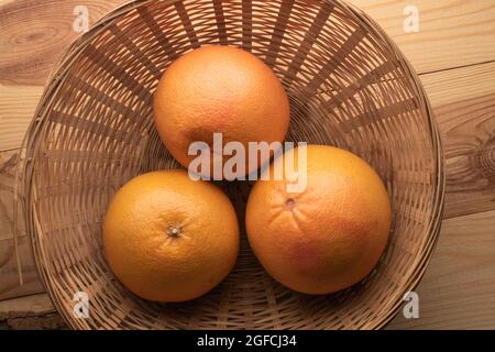 Tre pompelmo biologico succoso in una ciotola di paglia, primo piano, su un tavolo di legno, vista dall'alto. Foto Stock