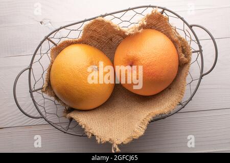 Due succose pompelmi biologici in un cestino, primo piano, su un tavolo di legno bianco, vista dall'alto Foto Stock