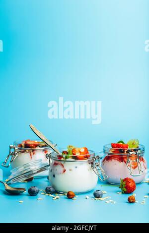 Yogurt con muesli, bacche fresche e noci in un vasetto su sfondo blu. Colazione sana e concetto di dessert al latte. Bella foto di cibo luminoso. Foto di alta qualità Foto Stock