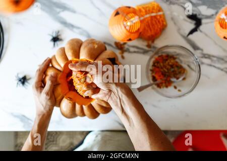 Un primo piano della mano dell'uomo tira semi e materiale fibroso da una zucca prima di intagliare per Halloween. Jack-o-lanterna. Vista dall'alto Foto Stock