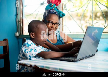 Felice madre africana della famiglia seduta al tavolo con suo figlio usando un calcolatore che sorride insieme Foto Stock