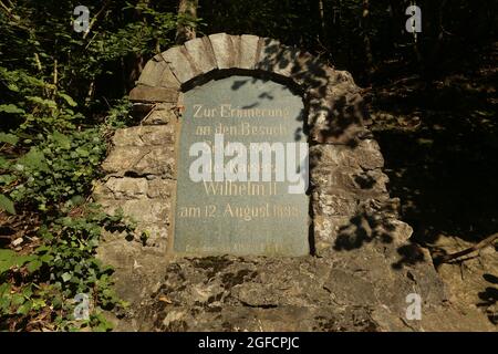 Solingen, Germania. 25 ago 2021. Una pietra commemorativa accanto al Ponte Müngsten commemora la visita del Kaiser Guglielmo II nel 1899. Il ponte ferroviario, un ponte a traliccio in acciaio, conduce su una valle del Wupper. La costruzione fu completata nel 1897 e fu chiamata 'Kaiser-Wilhelm-Brücke' fino al 1918. L'imponente struttura è la proposta della Renania settentrionale-Vestfalia di un elenco di domande per i futuri siti del Patrimonio Mondiale alla Conferenza dei Ministri della Cultura. Credit: David Young/dpa/Alamy Live News Foto Stock