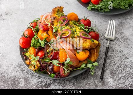 Omelette con verdure stufate e salmone, pomodori con cipolle, broccoli e pesce rosso con micrograni di piselli, deliziosa e abbondante colazione Foto Stock