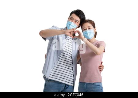 Giovane coppia con maschera chirurgica che fa la forma del cuore con le mani Foto Stock