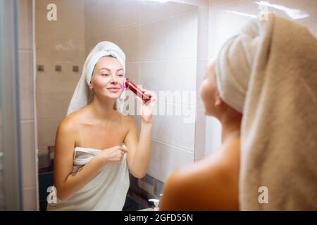 Elettroporazione portatile. Cura della pelle sollevamento spa e cosmetologia a casa. La ragazza fa microcircorrenti in bagno Foto Stock