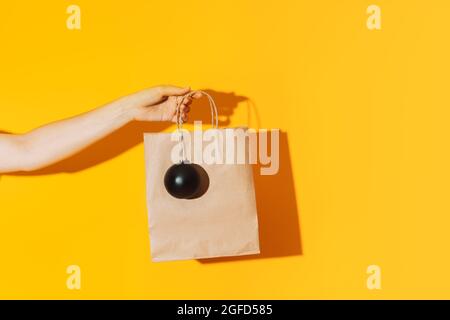 Sacchetto di carta con mano e sfera nera opaca su sfondo giallo Foto Stock