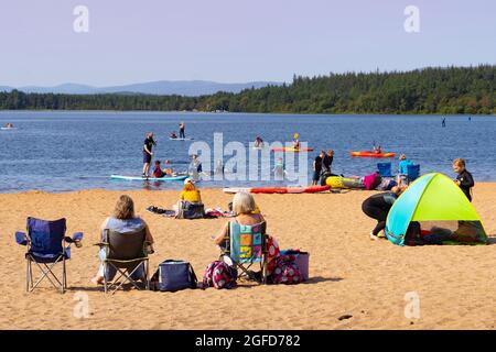 Aviemore, Scozia, Regno Unito. 25 agosto 2021. Il sole e le alte temperature di oltre 22 °C hanno portato gli appassionati di sport acquatici e gli amanti del sole al famoso centro di sport acquatici e alla spiaggia di Loch Morlich nel Glenmore Forest Park, nel Cairngorms vicino ad Aviemore, nelle Highlands scozzesi. Iain Masterton/Alamy Live News. Foto Stock