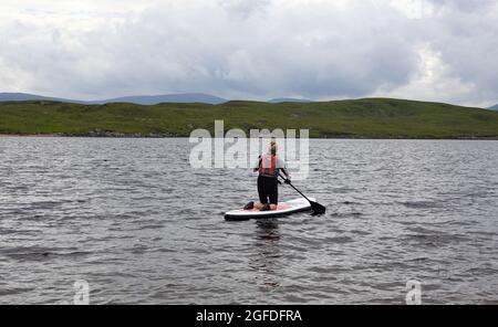 Signora anziana inginocchiata su Stand up paddle Board, Loch Laidon, Perthshire Scottish Highlands, Regno Unito Foto Stock