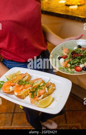 Cameriera donna che tiene in lei un vassoio di legno con bruschetta mano Foto Stock