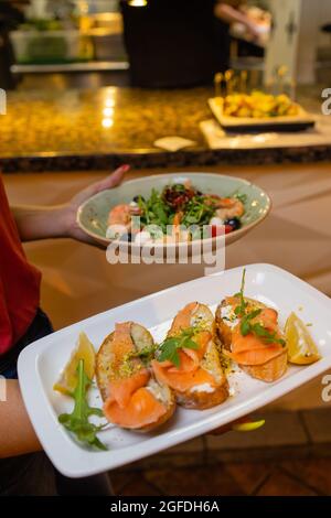 Cameriera donna che tiene in lei un vassoio di legno con bruschetta mano Foto Stock