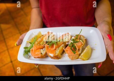 Cameriera donna che tiene in lei un vassoio di legno con bruschetta mano Foto Stock