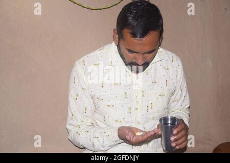 Giovane rurale con pillole e bicchiere d'acqua nelle sue mani, sta per prendere qualche medicina, periodo Corona Foto Stock