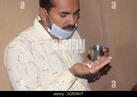 Giovane rurale con pillole e bicchiere d'acqua nelle sue mani, sta per prendere qualche medicina, periodo Corona Foto Stock