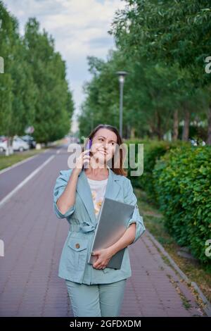 una ragazza allegra che cammina per la città con un computer portatile Foto Stock