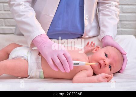 Il medico controlla la temperatura del neonato con un termometro. Un infermiere in uniforme misura la febbre del bambino con un termometro Foto Stock