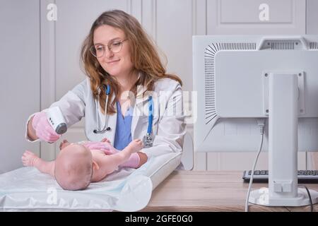 Il medico controlla la temperatura del neonato con un termometro. Un infermiere in uniforme misura la febbre del bambino con un termometro Foto Stock