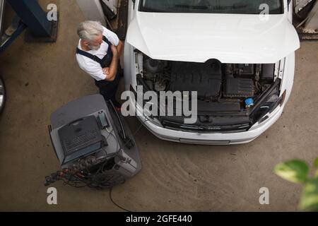 Vista dall'alto di un esperto addetto al servizio di assistenza auto che esamina l'auto sotto il cofano Foto Stock