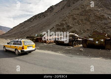 Un taxi afghano guida di fronte ai vecchi carri armati russi che sono il residuo dell'invasione sovietica dell'Afghanistan nella provincia di Panjshir, Afghanistan il 02 gennaio 2010. (STATI UNITI Foto dell'esercito di Sgt. Teddy Wade/rilasciato) Foto Stock