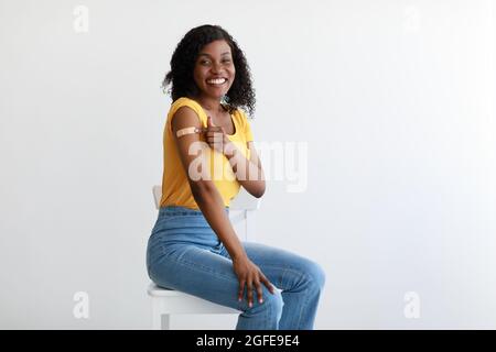 Vaccinato African American Woman mostrando Arm con intonaco, sfondo grigio Foto Stock