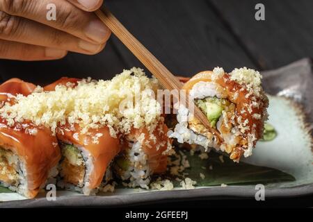 primo piano di bacchette nelle mani degli uomini prendere parte del rotolo di sushi sul ristorante al tavolo / mangiare rotolo di sushi usando bacchette Foto Stock