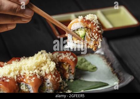 primo piano di bacchette nelle mani degli uomini prendere parte del rotolo di sushi sul ristorante al tavolo / mangiare rotolo di sushi usando bacchette Foto Stock