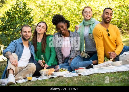 Portrait of smiling young friends having picnic in public park Foto Stock