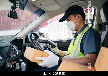 Addetto alla consegna asiatico che utilizza un lettore di carte di credito. In auto con pacchi all'esterno del magazzino. Consegna Foto Stock