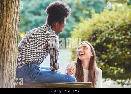 Sorridendo i giovani amici che si guardano mentre si siedono sulla panca Foto Stock
